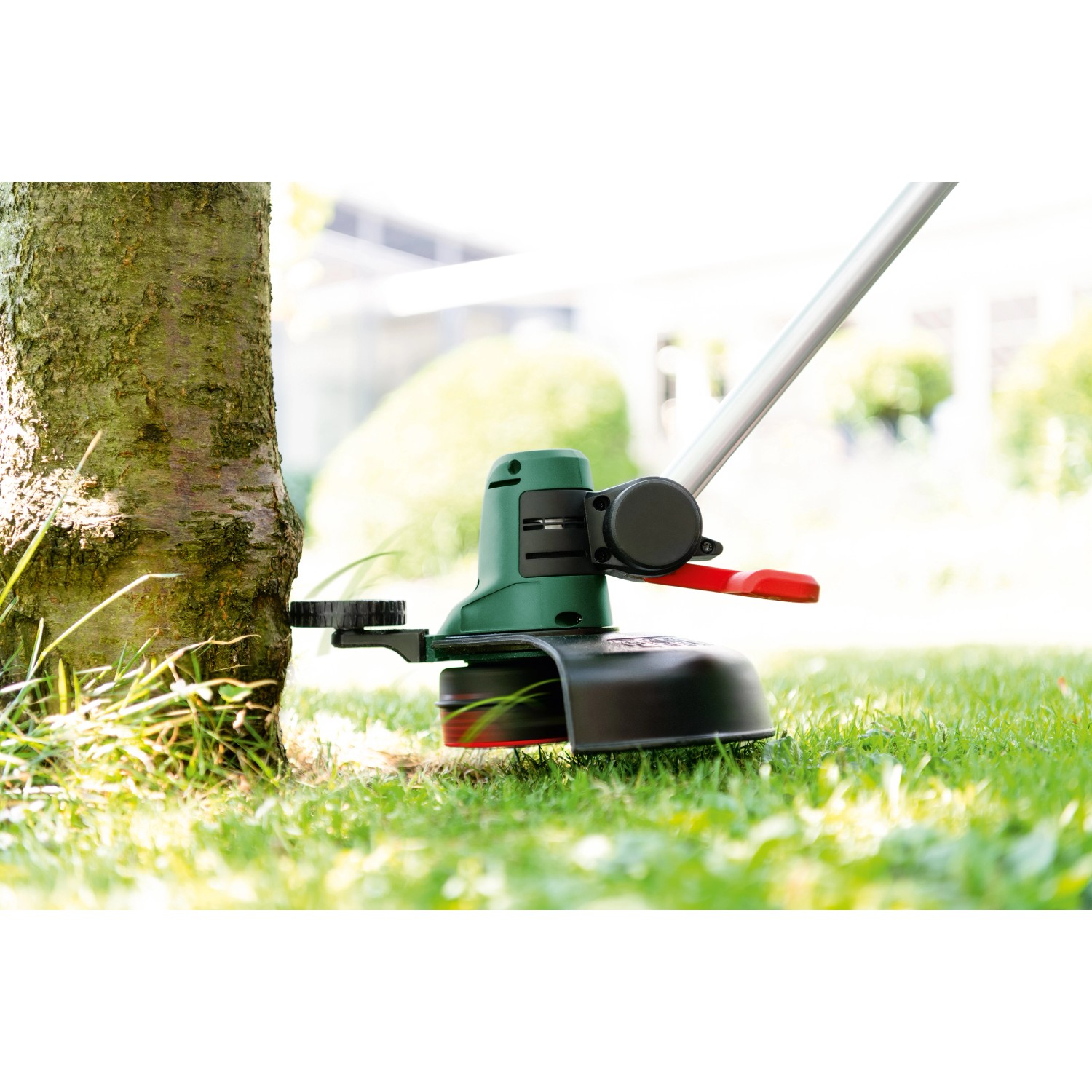 Bosch Akku-Rasentrimmer UniversalGrassCut 18V-26 beim Trimmen von Gras um einen Baum.