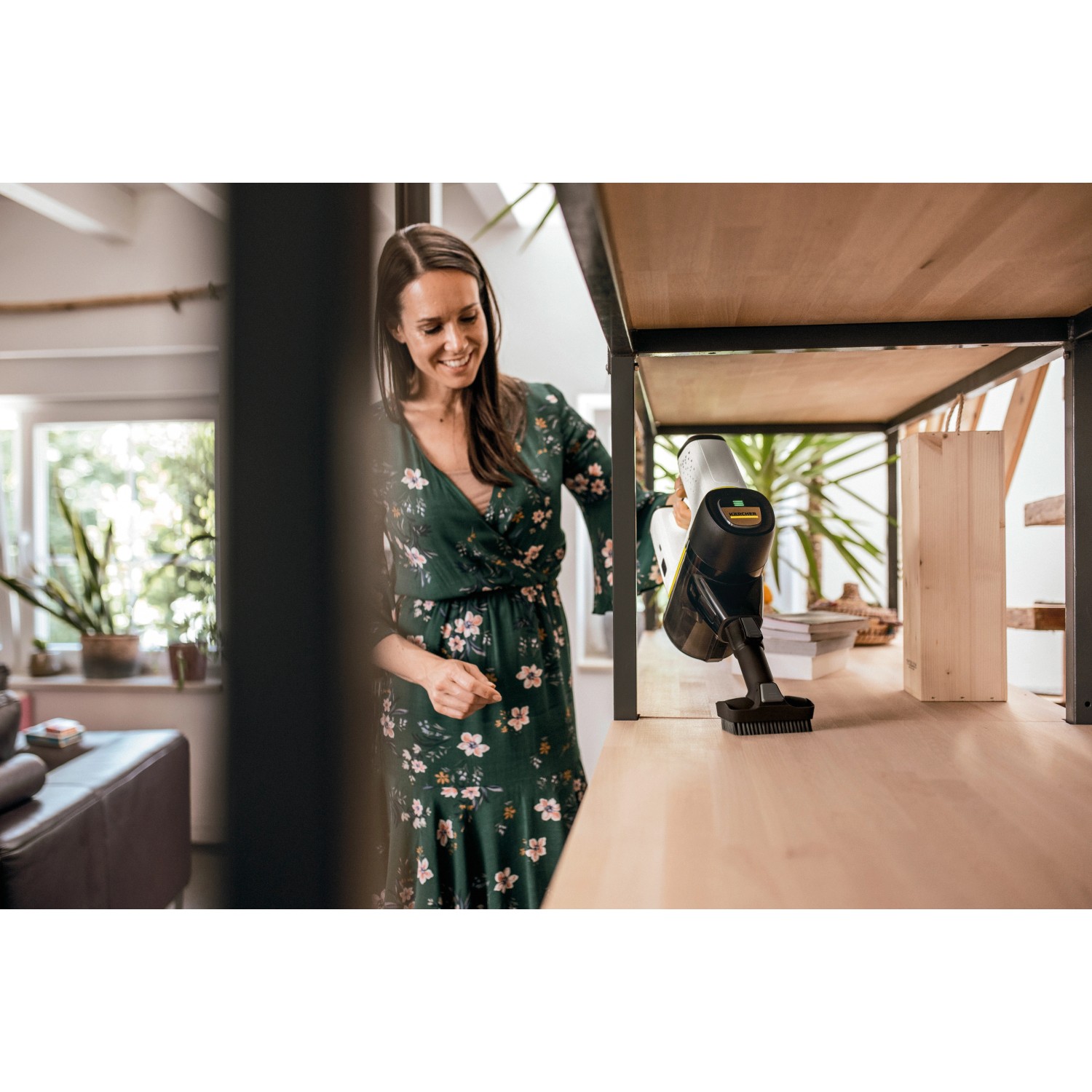 Frau saugt Regal mit Kärcher Akku-Staubsauger VC 6. Kabelloser Bodenstaubsauger mit Akku.