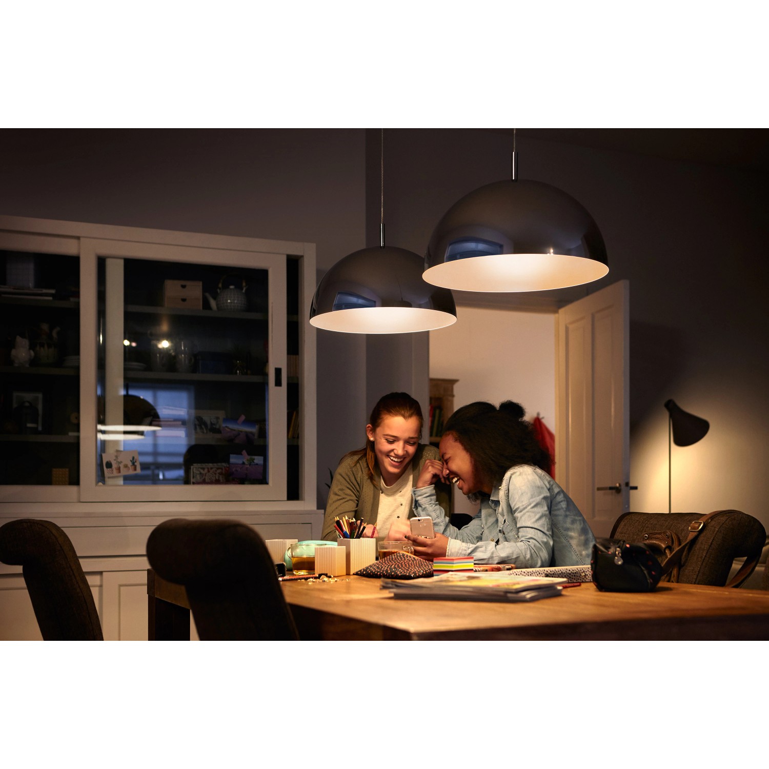 Szene mit Philips E27 LED-Lampen (3er Set) in Glühlampenform über einem Esstisch, der von zwei Mädchen genutzt wird.