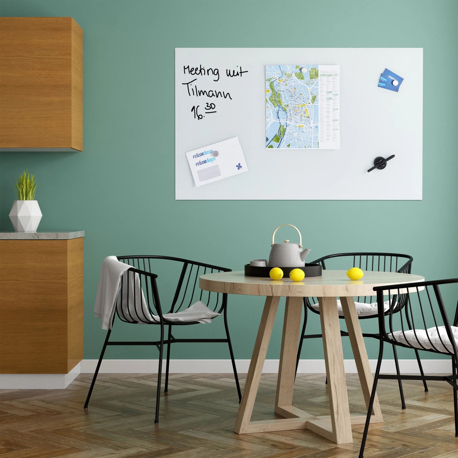 Weißes Relaxdays Glas Magnetboard 100x60 cm an grüner Wand mit Notizen. Ideal für Büro und Küche.