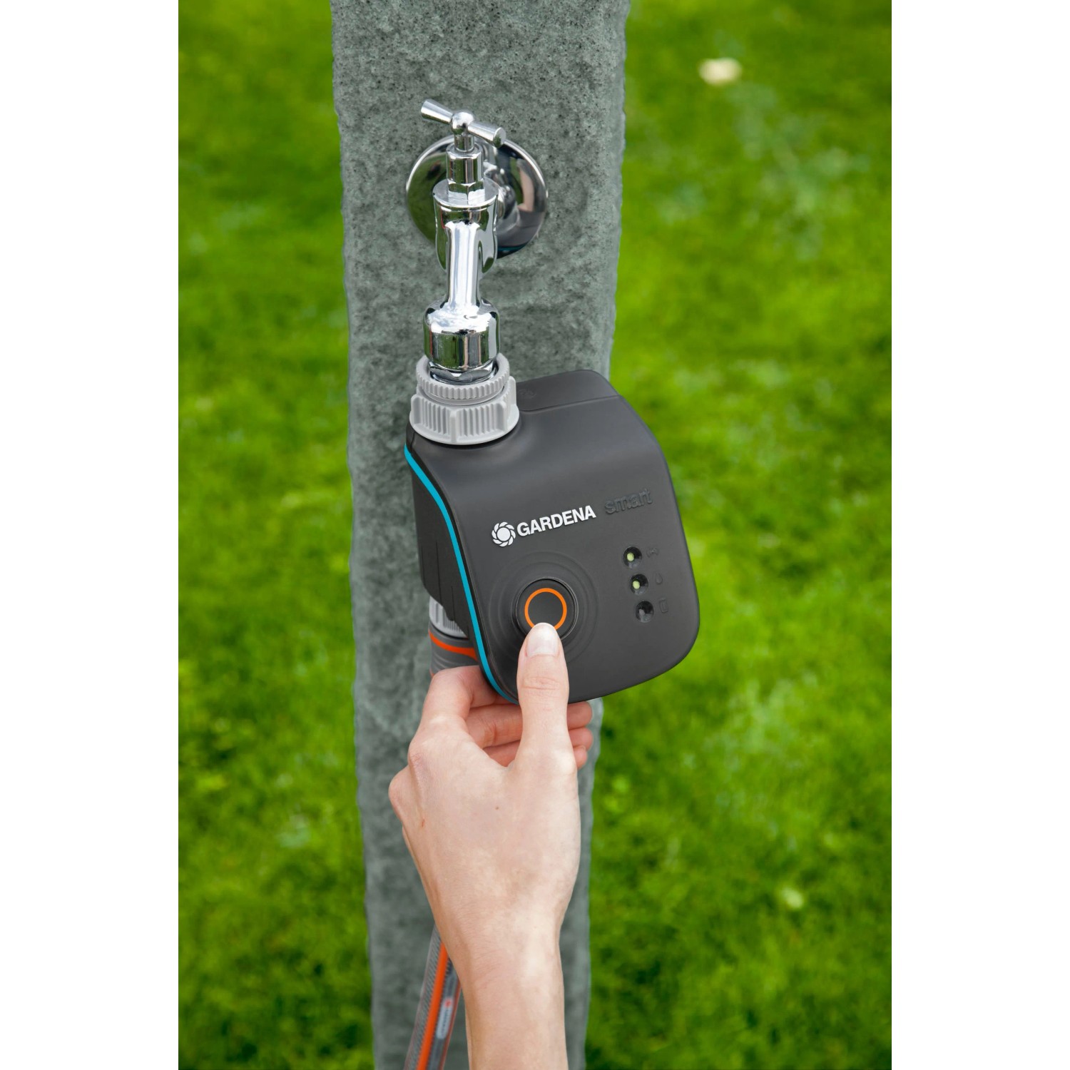 Gardena smart Water Control Bewässerungscomputer am Wasserhahn mit Hand, die den Knopf drückt.