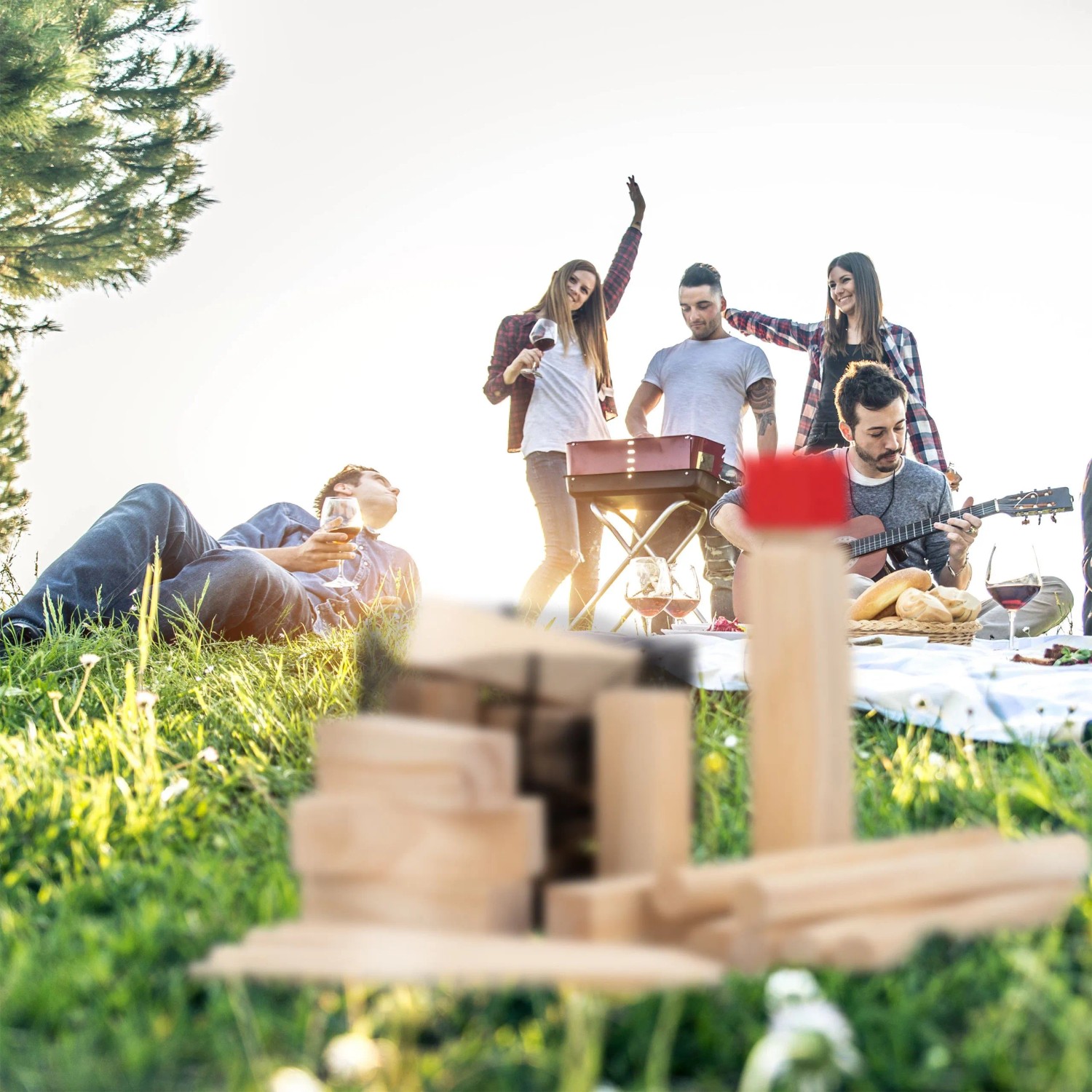 Kubb Wikingerspiel aus Natur-Kiefernholz mit rotem König im Vordergrund, Freunde spielen im sonnigen Garten.