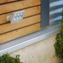Silberne Briloner LED-Außenwandleuchte Lero mit Bewegungsmelder an einer Holzwand.