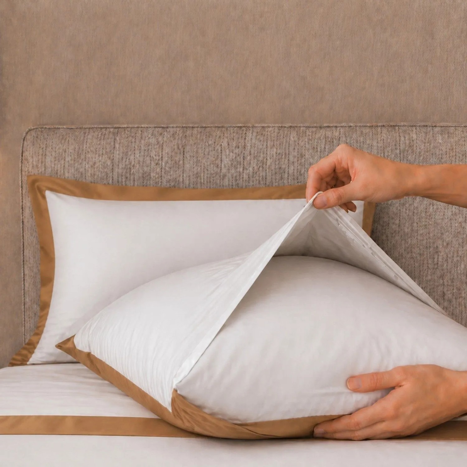 Hände beziehen weißes Baumwoll-Kissen mit beiger Satin-Bordüre. Bettwäsche-Set Doppelbett.