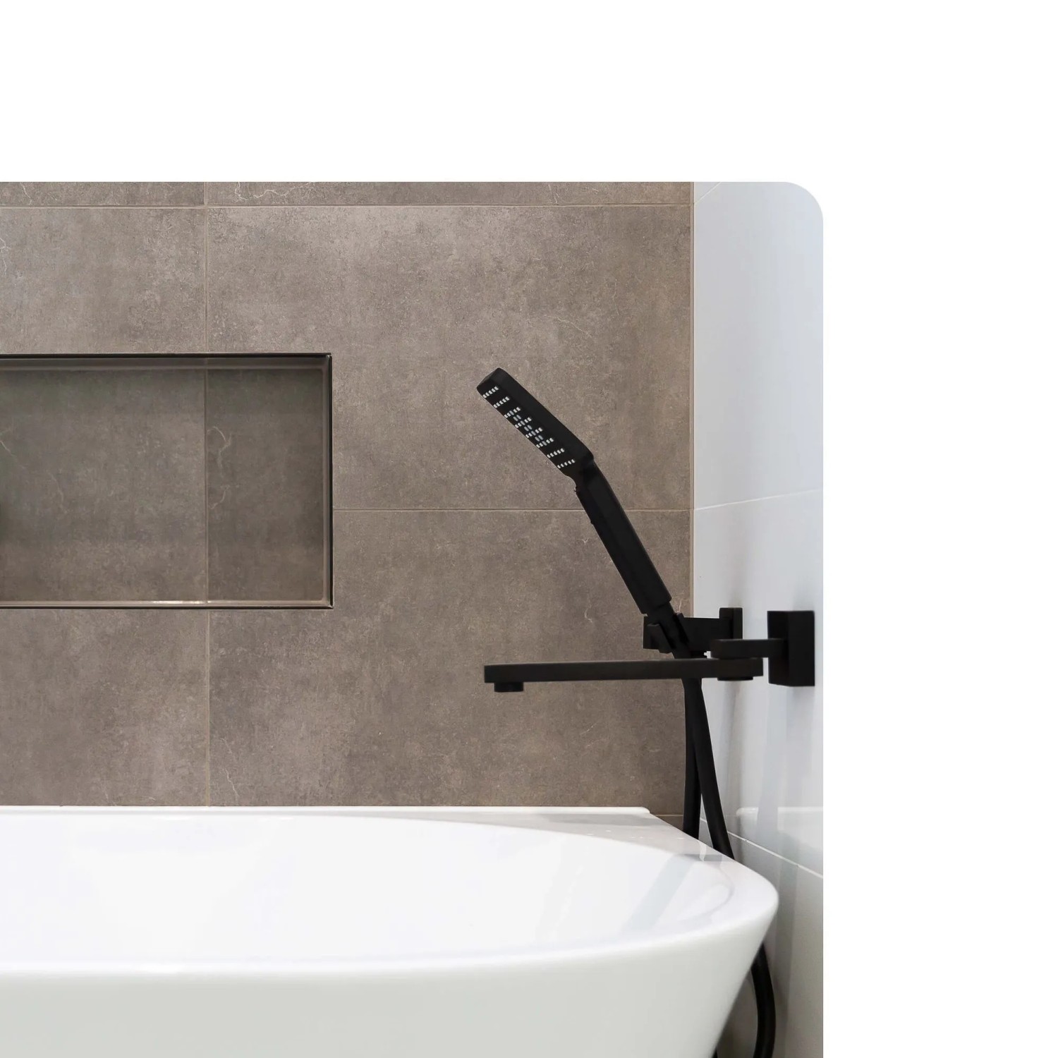 Eingebaute Badewanne mit schwarzer Dalsys Armatur vor grauen Fliesen. 