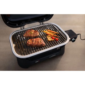 Weber Lumin Elektro-Tischgrill, schwarz, mit Steaks und Gemüse auf dem Grillrost.