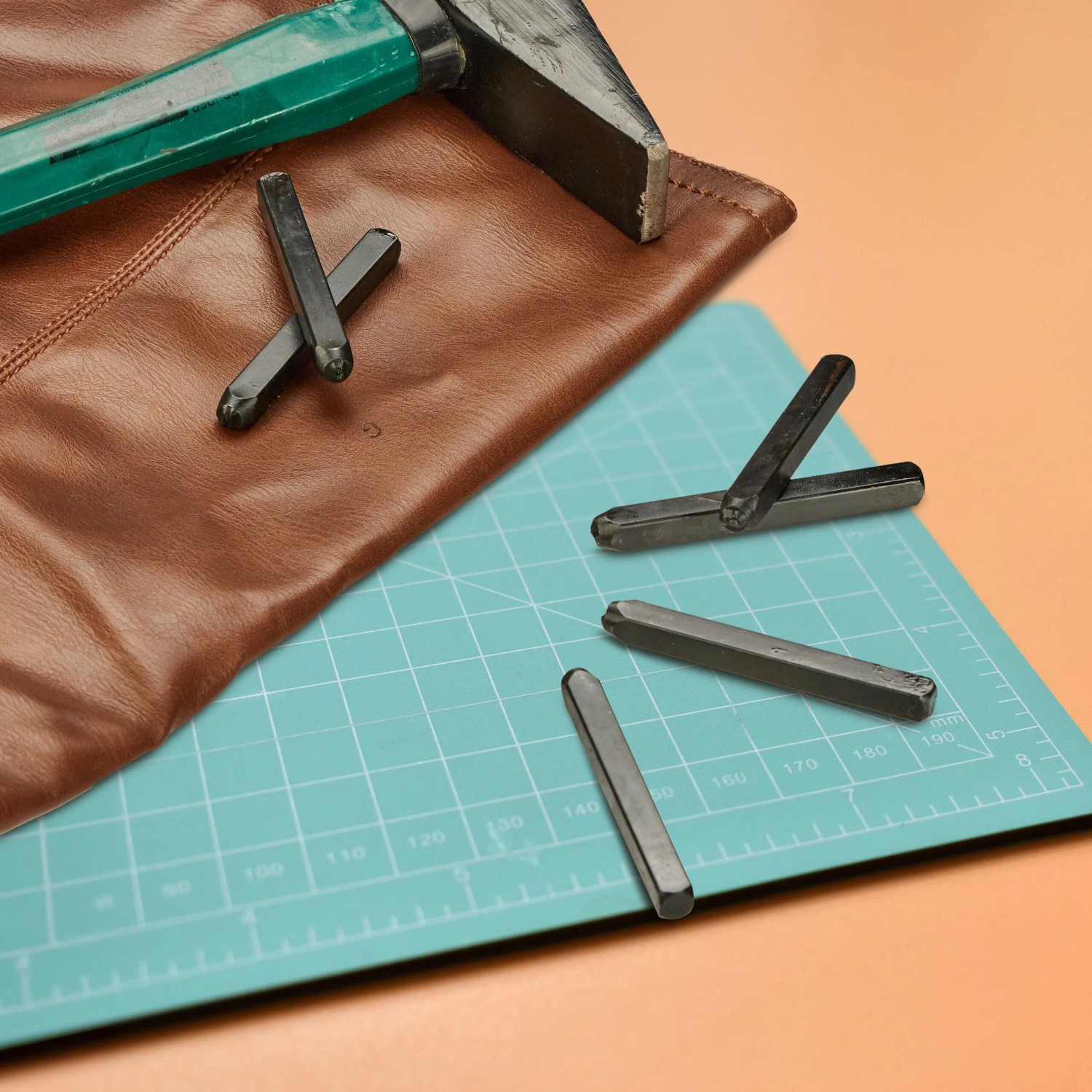 Schlagbuchstaben aus schwarzem Stahl, Hammer und Leder auf Schneidematte. Ideal für Prägearbeiten und DIY-Projekte.