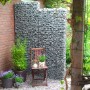 Gabiona Gabionenzaun (100x52x17 cm) gefüllt mit Steinen im Garten, dekoriert mit Pflanzen und Stuhl.