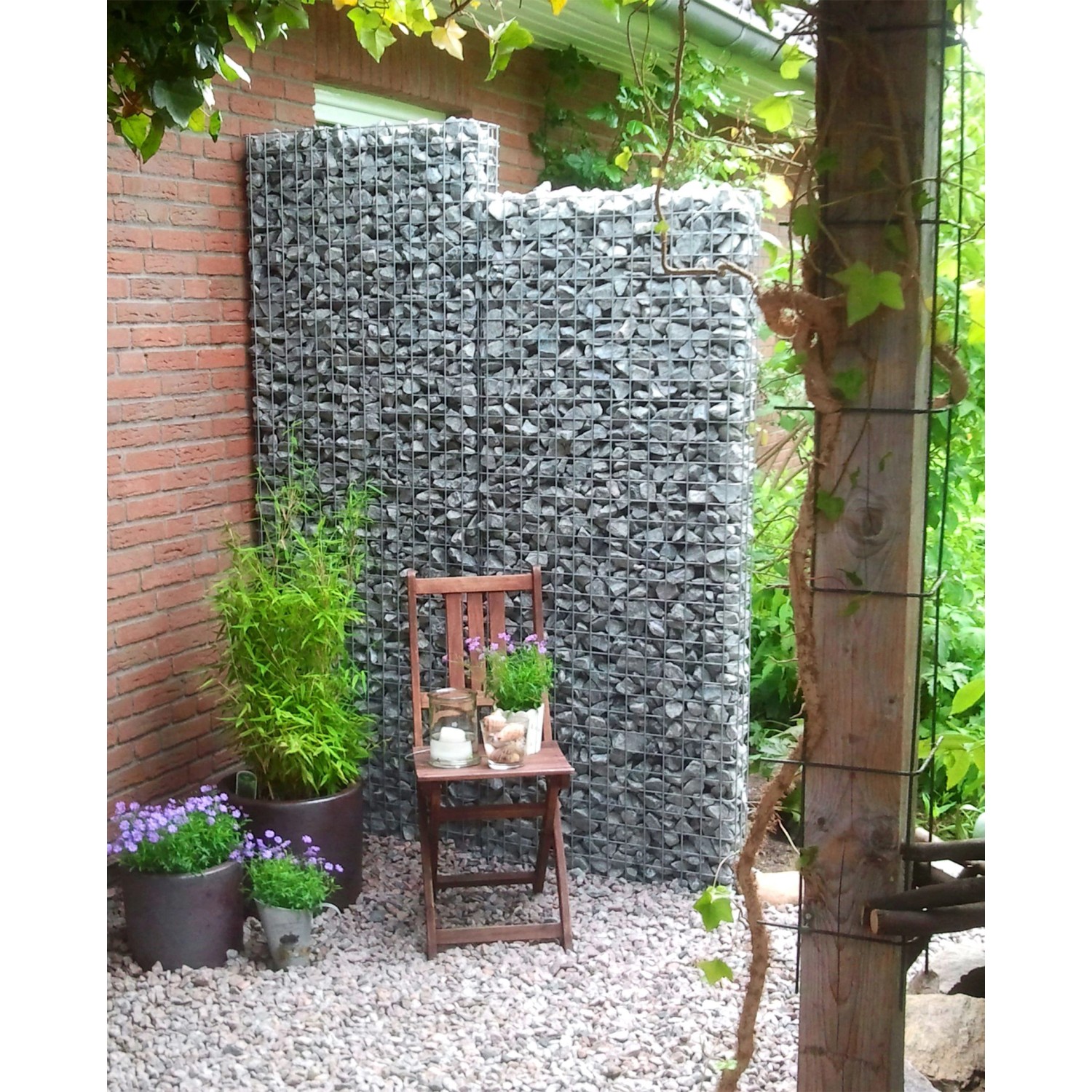 Gabiona Gabionenzaun (100x52x17 cm) gefüllt mit Steinen im Garten, dekoriert mit Pflanzen und Stuhl.