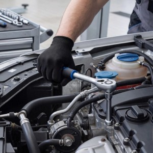 Hand mit schwarzem Handschuh nutzt Ratschenschlüssel am Auto-Motor. Wiltec 108-teiliger Steckschlüsselsatz für Reparaturen.