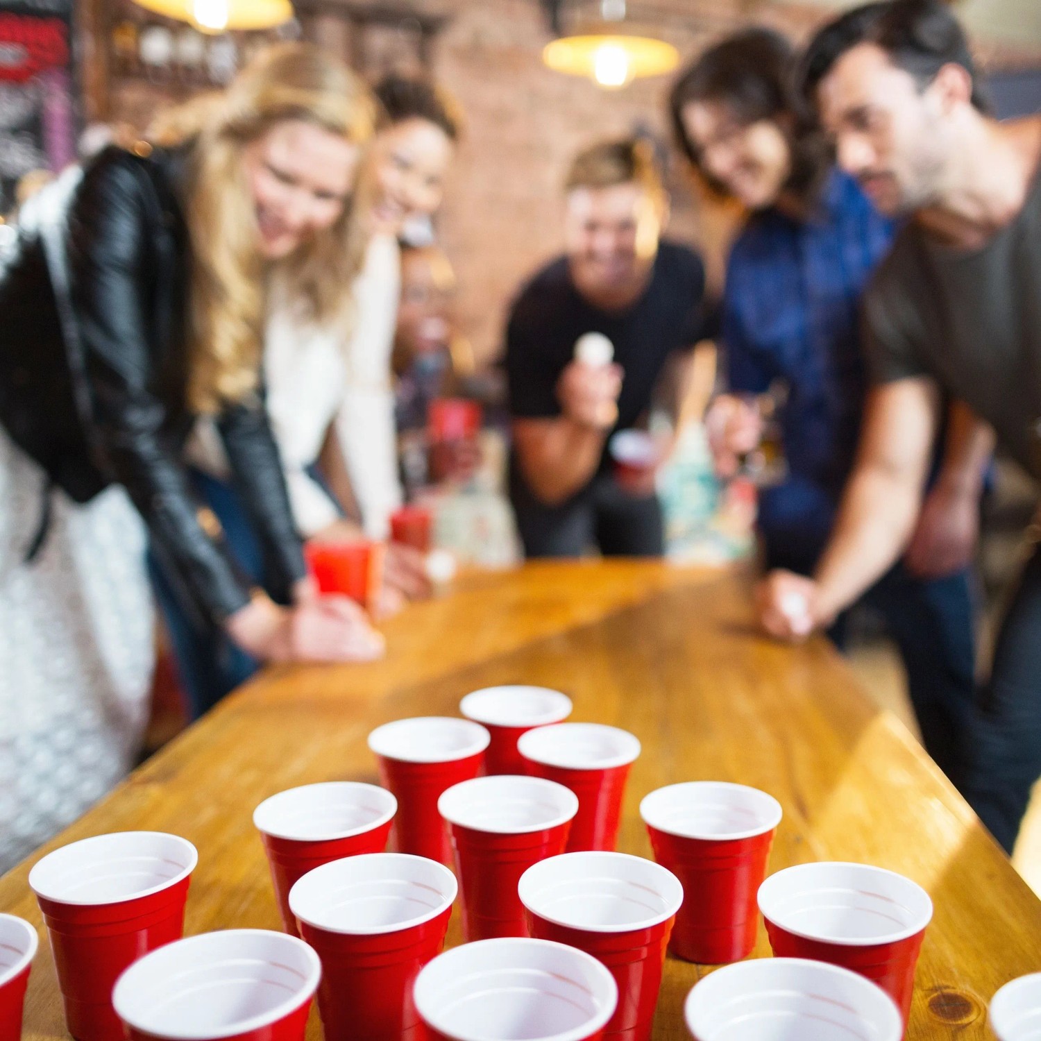 Fröhliche Freunde spielen Bierpong mit roten Kunststoffbechern und Bällen auf einem Holztisch. Das Bierpong Set für Partys.