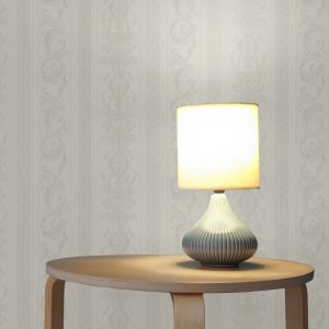 Tadessi Vliestapete in Creme mit barockem Ornament und Streifenmuster an einer Wand, beleuchtet von einer Lampe.
