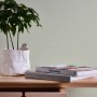 A.S. Création Vliestapete Uni Grün an Wand mit Tisch, Pflanze und Büchern.