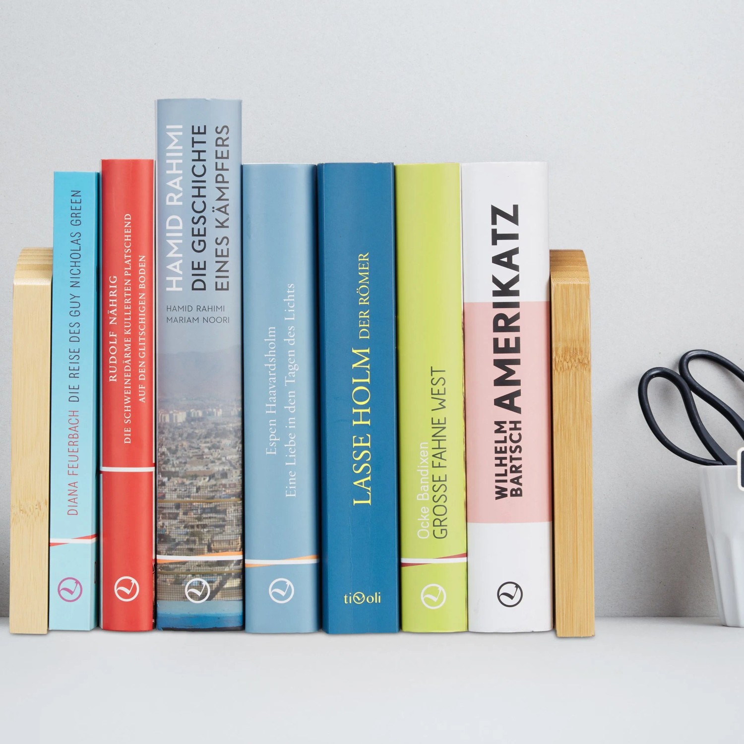 Zwei moderne Buchstützen aus hellem Bambus und Edelstahl halten bunte Bücher aufrecht. Ideal für Büro & Schreibtisch.