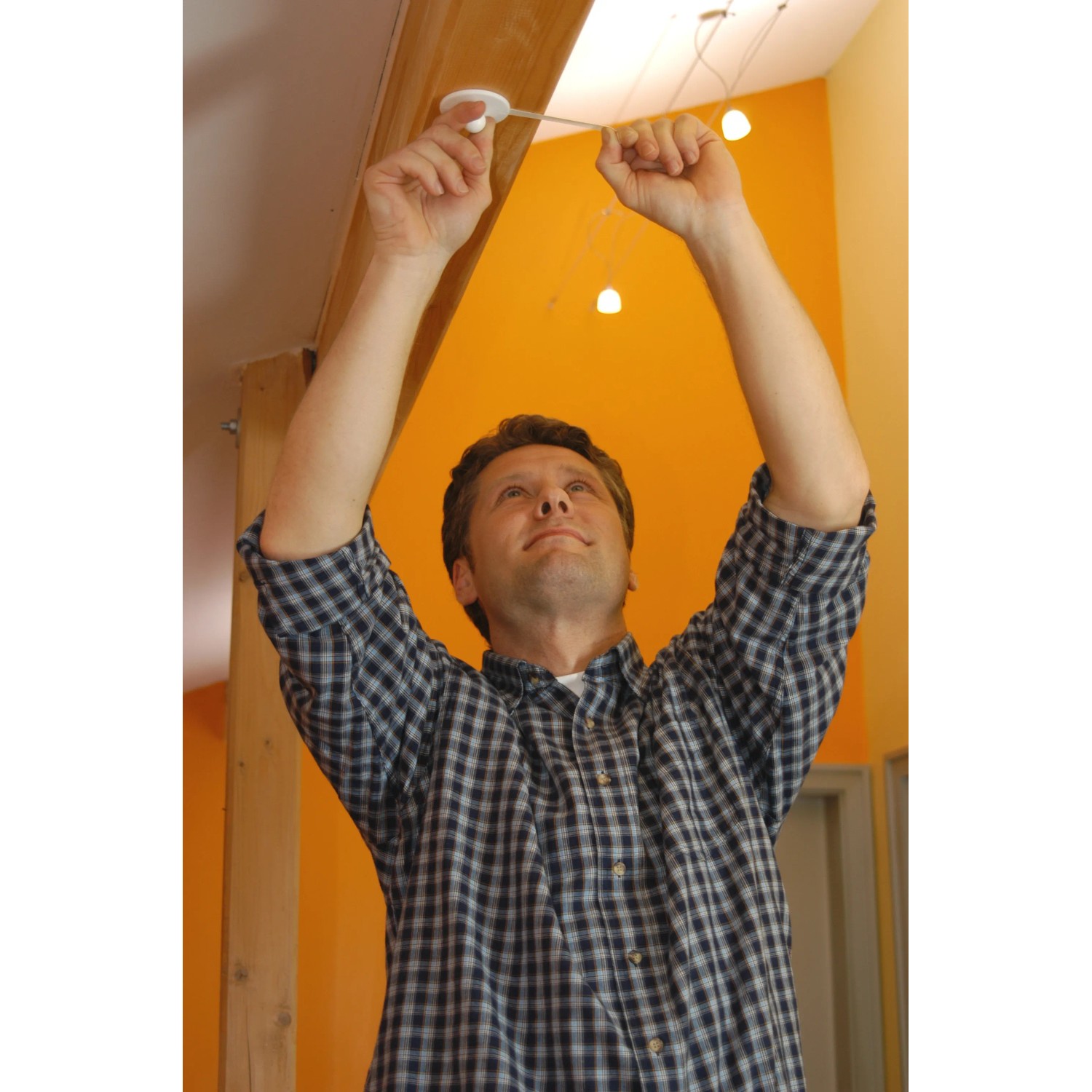 Mann befestigt Tesa Powerstrips Deckenhaken an Decke, um Lampe aufzuhängen.