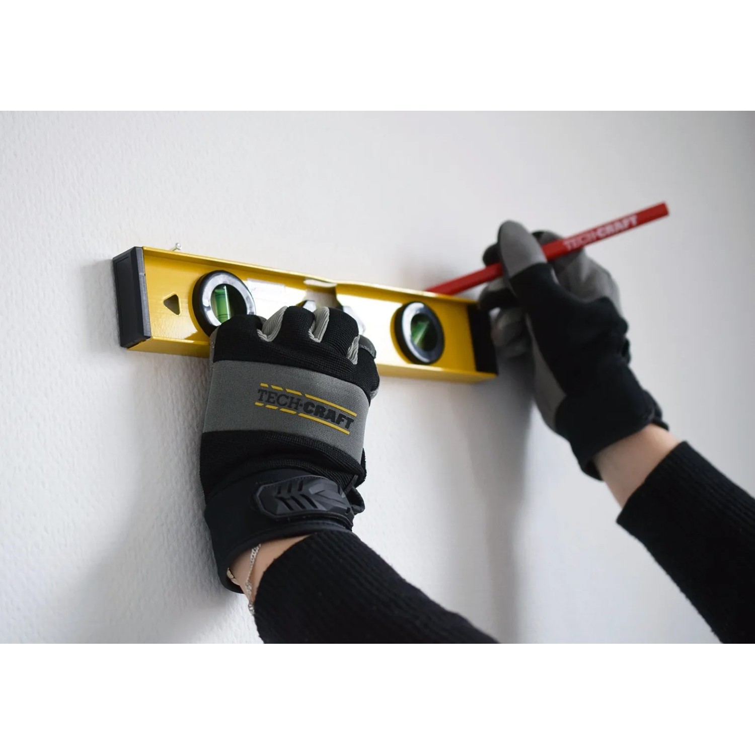 TECH-CRAFT Wasserwaage in Nutzung mit Handschuhen und Stift an einer Wand.