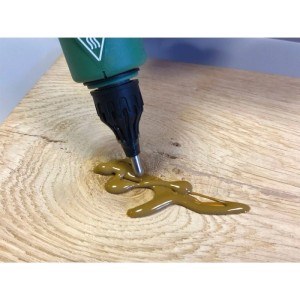Grüne Astfüller-Pistole trägt kieferfarbenen Wood-Repair Stick auf Holz auf, füllt Risse und Löcher präzise.