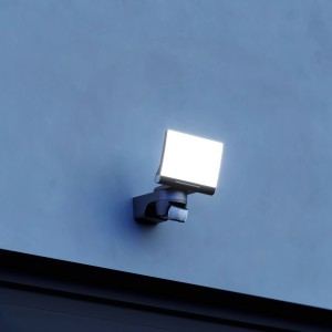 Schwarzer Steinel LED-Strahler XLED Home 2 SC mit Bewegungsmelder an blauer Wand.