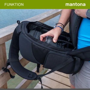 Mantona Trekking Fotorucksack mit Rückenöffnung. Person verstaut Kameraobjektiv. Sicherer Stauraum für Fotoausrüstung.