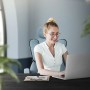 Frau sitzt auf blauem, ergonomischem ML-Design Bürostuhl mit hoher Rückenlehne vor Laptop.