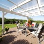 Weiße Skan Holz Terrassenüberdachung Ancona aus Leimholz mit Polycarbonatplatten und Sitzgruppe im Garten.