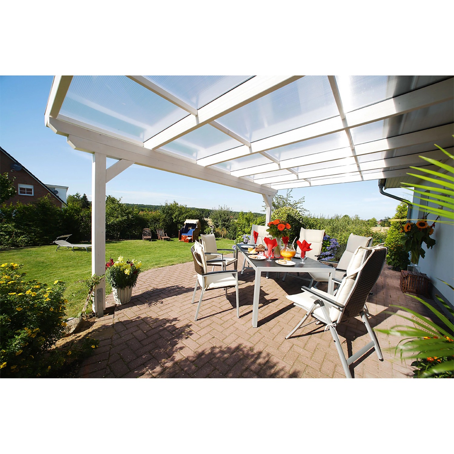 Weiße Skan Holz Terrassenüberdachung Ancona aus Leimholz mit Polycarbonatplatten und Sitzgruppe im Garten.