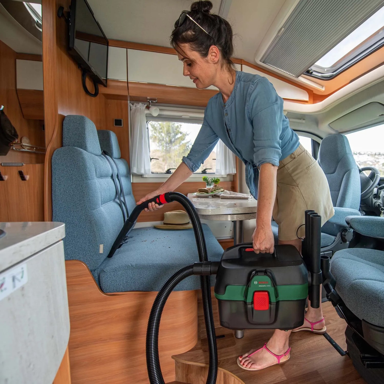 Frau saugt mit Bosch Akkusauger AdvancedVac 18V-8 Polster im Wohnmobil. Nass- & Trockensauger mit Zubehör.