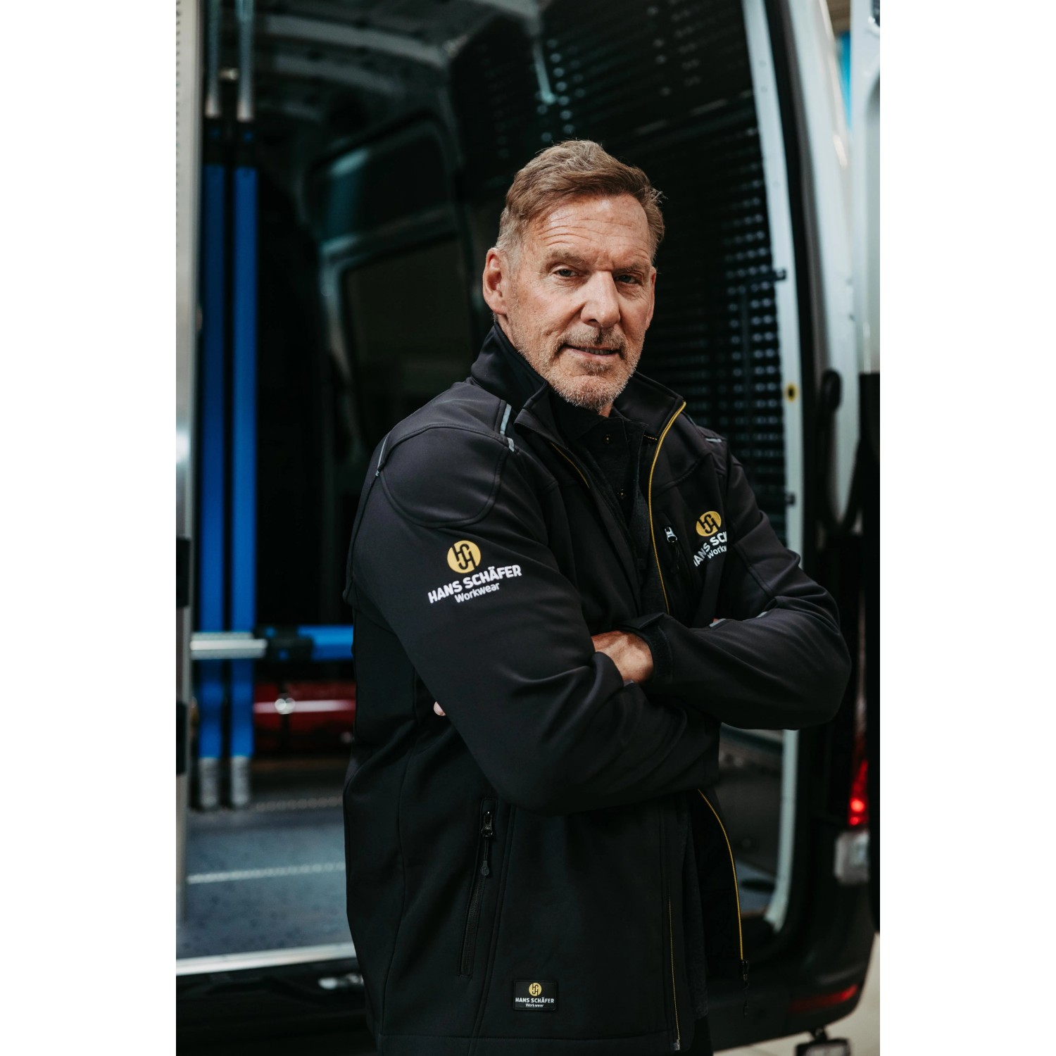 Mann mit Hans Schäfer Workwear Softshelljacke in Schwarz, Größe M, vor Transporter. Arbeitskleidung.
