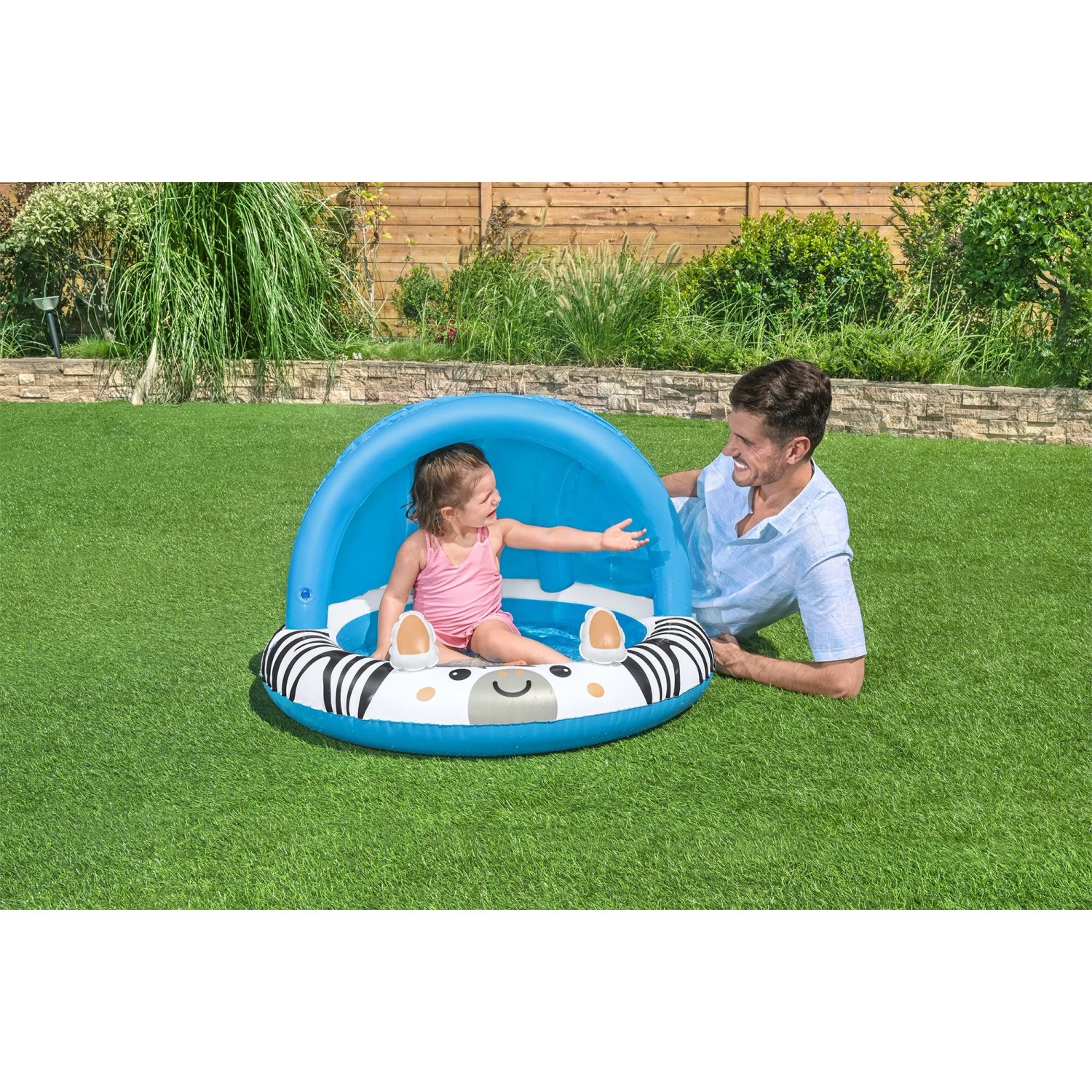 Bestway Planschbecken Safari Sun mit Sonnendach, Zebra-Design, Kind sitzt im Pool, Erwachsener liegt daneben.
