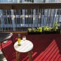 Rot gemusterter Primaflor Rasenteppich auf einem Balkon mit Tisch und Stuhl.