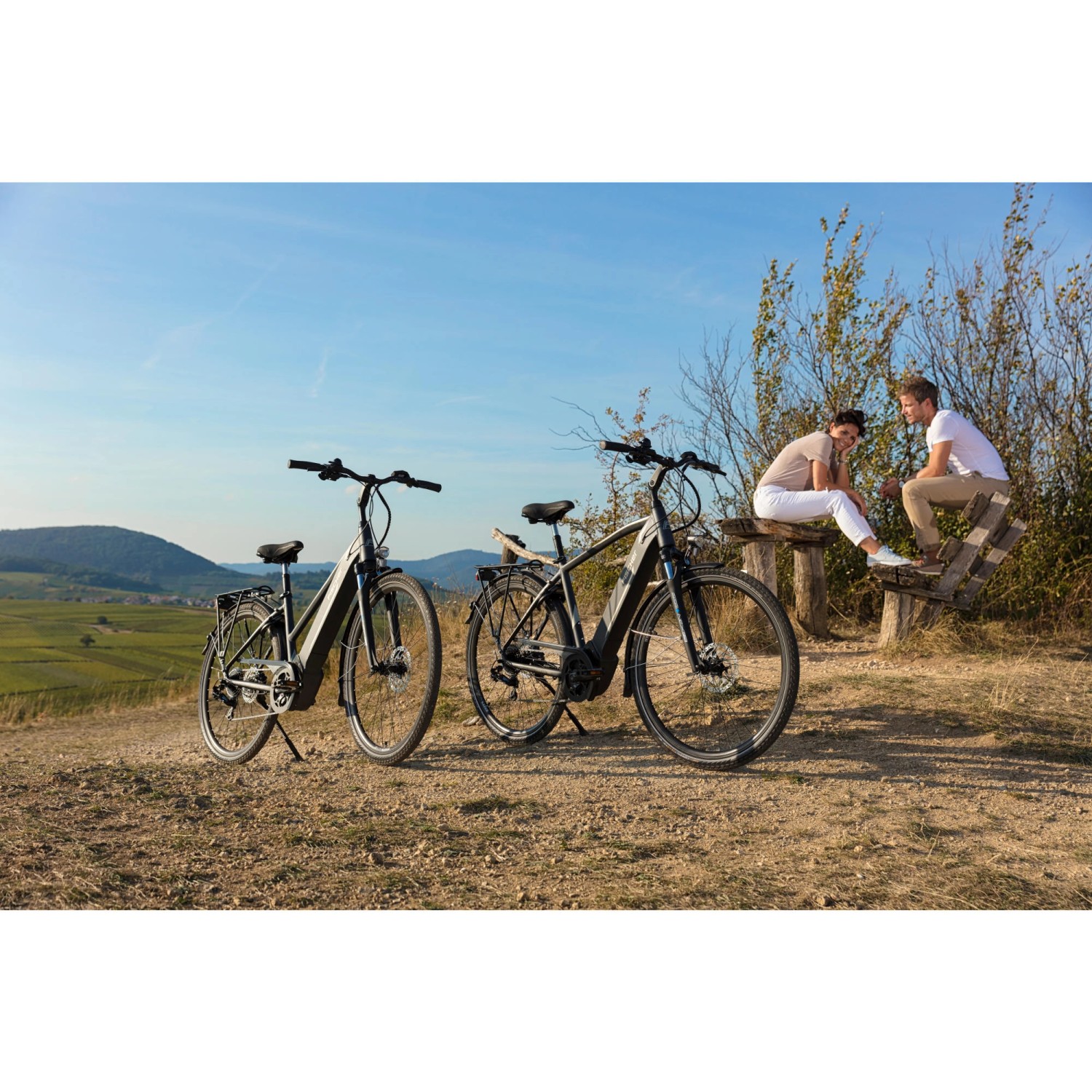 Zwei Fischer E-Bikes Viator 5.0i vor Landschaft. Paar sitzt auf Bank.