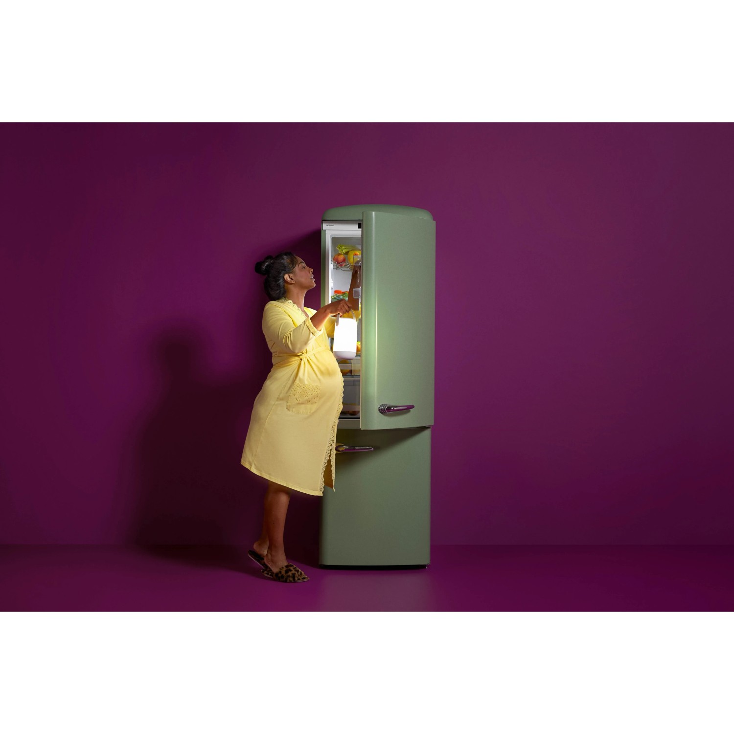 Frau öffnet grünen Kühlschrank, beleuchtet durch WiZ Smart LED Leuchte.