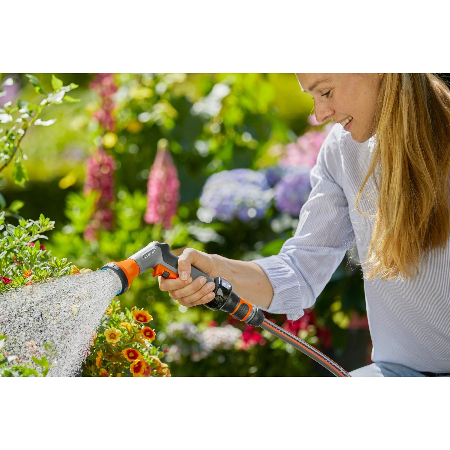 Frau bewässert Blumen mit Gardena Bewässerungsbrause AquaCount im Garten.