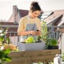 Frau mit Lechuza Balconera Stone 50 Blumenkasten in Steingrau auf Balkon mit Bepflanzung.