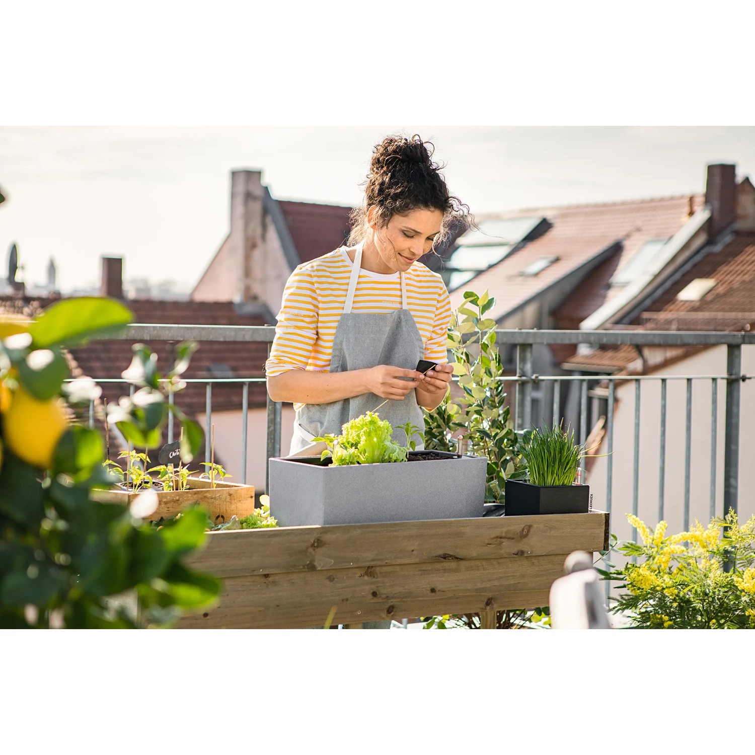 Frau mit Lechuza Balconera Stone 50 Blumenkasten in Steingrau auf Balkon mit Bepflanzung.
