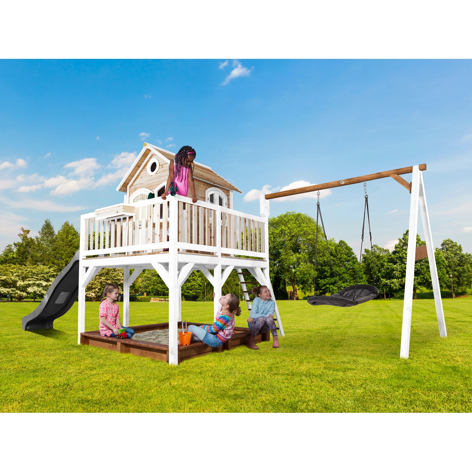 Axi Liam Spielhaus mit Roxy Nestschaukel, braun-weiß mit grauer Rutsche und Sandkasten. Kinder spielen im Garten.