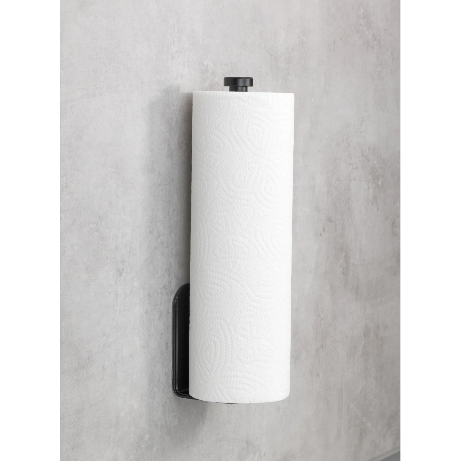 Wenko Küchenrollenhalter Nio, selbstklebend, schwarz mit Küchenrolle an grauer Wand.