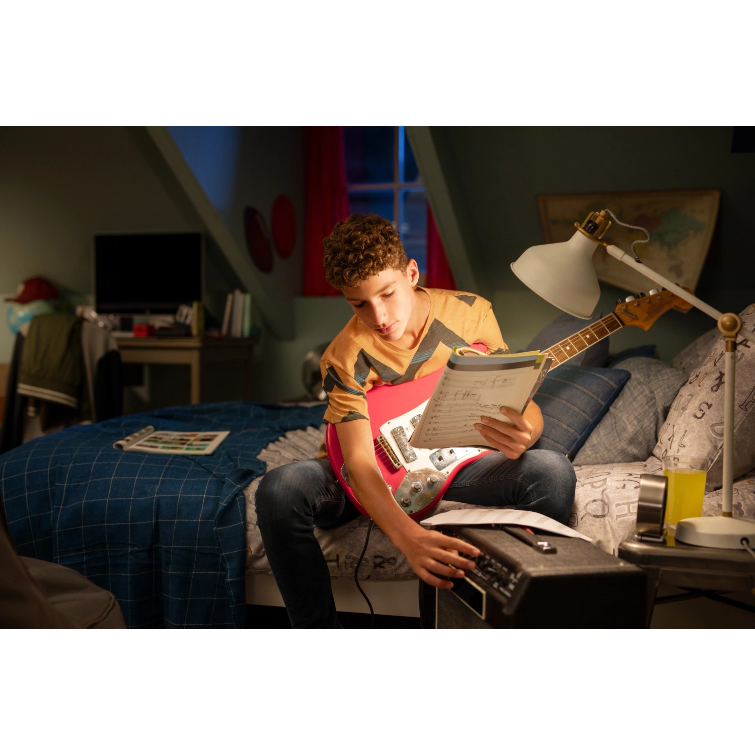 Junge spielt E-Gitarre im Zimmer, beleuchtet mit Philips LED Lampe. Fokus auf entspannte Atmosphäre mit LED-Beleuchtung.