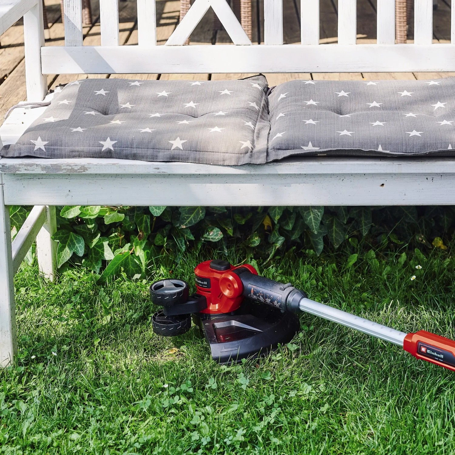 Einhell Akku-Rasentrimmer GE-CT 18/30 Li-Solo unter einer Gartenbank auf Rasen.
