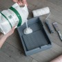 Wallpro Werkzeug-Set für Vliestapeten: Kleister wird in eine Farbwanne gegossen, mit Rolle und Pinsel.