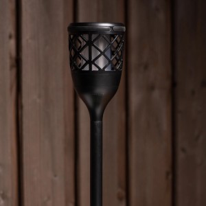 Schwarze Solar-Laterne Rapanui mit Erdspieß und Flammeneffekt vor Holzwand.