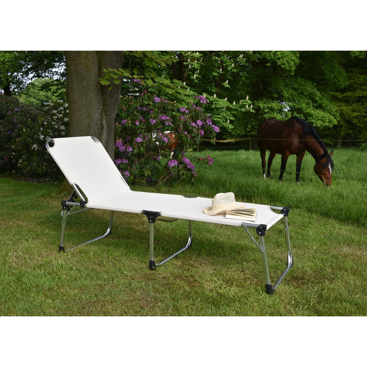 XXL Sonnenliege Abaco in Silber-Beige mit Hut und Buch im Garten.