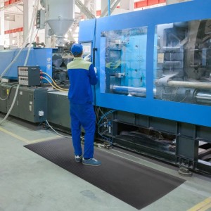 Schwarze KARAT Anti-Ermüdungsmatte Softer-Work-Mat 90x250cm vor Industriemaschine.