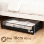 Schwarze Unterbettkommode mit transparentem Deckel und Rollen, gefüllt mit Textilien, unter einem Bett. Höhe 18cm.