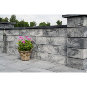 Diephaus Gartenmauer Pfeilerstein Weiß-Schwarz. Graue Mauer mit dunkler Abdeckung und Pfeiler, Blumenkorb auf Terrasse.