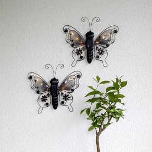 Zwei schwarze LED-Solar-Wanddeko Schmetterlinge aus Metall mit LED-Licht auf weißer Wand. Dekorative Solarleuchten.