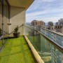 Balkon mit Primaflor Kunstrasen Cyprus: Grüner Kunstrasen mit Pflanze auf einem sonnigen Balkon.