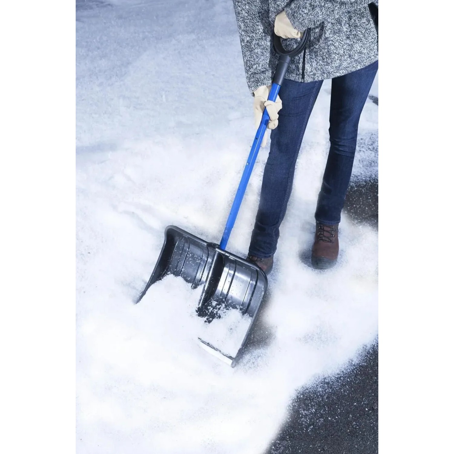 Person schiebt Schnee mit blauer Teleskop-Schneeschaufel aus Stahl und Kunststoff auf gepflastertem Weg.