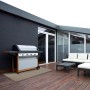 Wetterfester KARAT Outdoor Teppich Pavia, beige, 90x150 cm, auf einer Holzterrasse mit Grill und Gartenmöbeln.