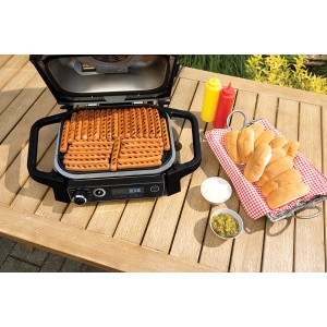Ninja Elektrogrill OG701DE mit Würstchen, Bötchen und Saucen auf einem Gartentisch.